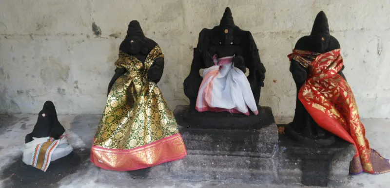 Four dark goddess idols in colourful saris against a wall