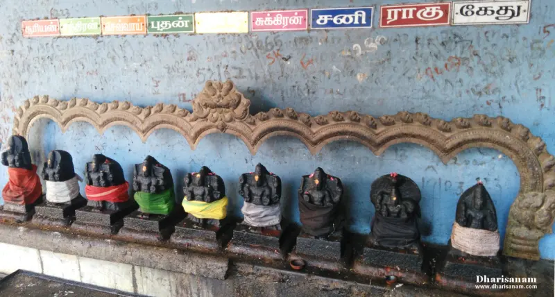 Nine small stone idols in a row on a ledge, with Tamil name boards above them.