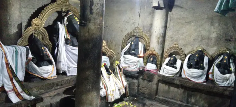 A row of dark stone Vinayakar images dressed in white cloth, each in front of a gilded arch.