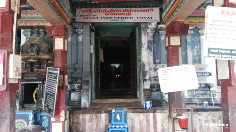 Doorway into a dark sanctum under a red Tamil name board, with notice boards at the sides