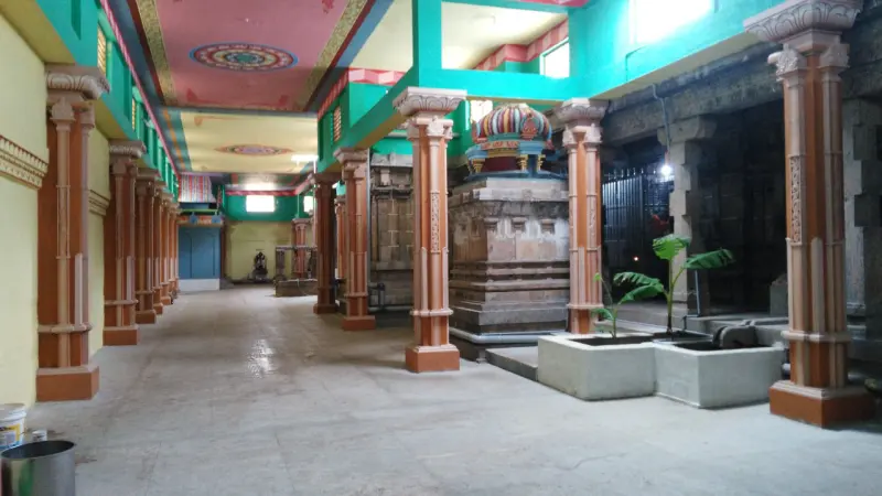 A hall of orange pillars with a small shrine roof and a young plantain plant in a planter.