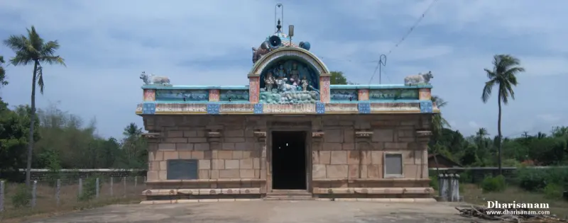Low stone shrine with a painted stucco figure above the doorway, with coconut palms behind
