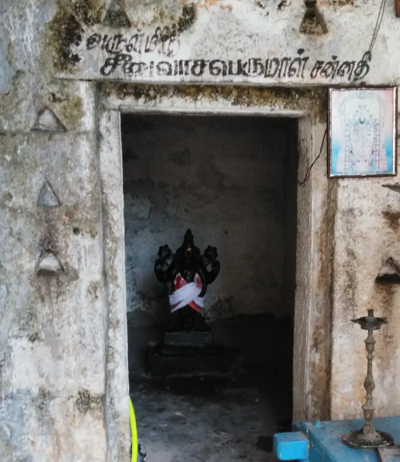 A plain stone doorway with a Tamil sign above it and a dark idol in white cloth inside