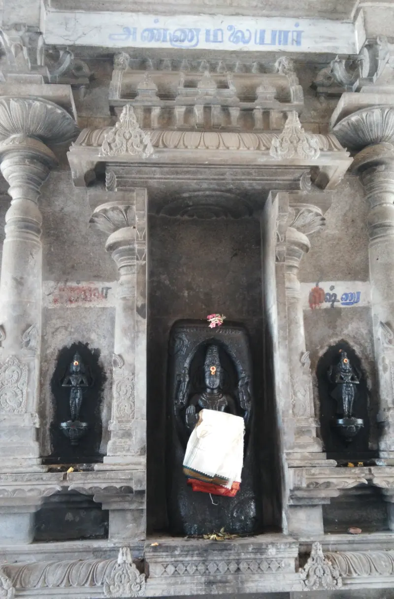 A standing black stone image in a niche with a smaller image on either side