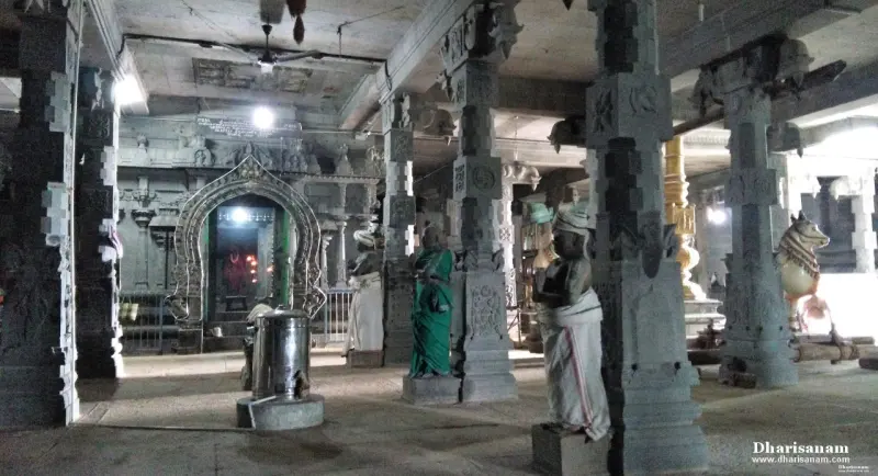A hall of carved stone pillars with statues, a Nandhi at right and a lit shrine entrance at the far end