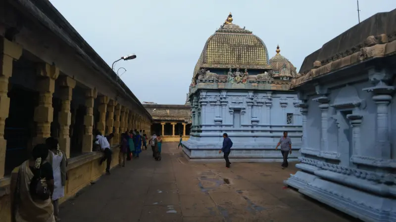A paved corridor with devotees walking, a blue shrine with a golden dome ahead.