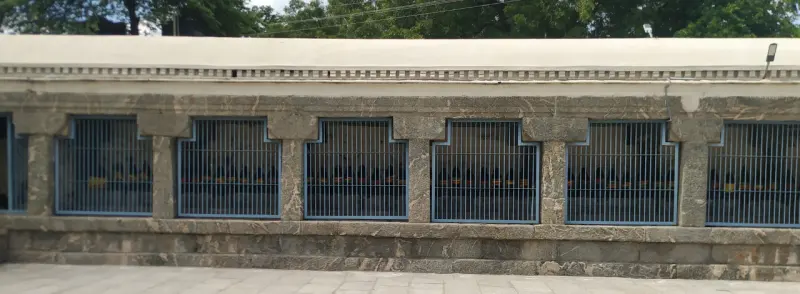 A long stone wall with a row of blue-framed barred windows above a paved floor.