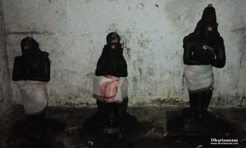Three black idols draped in white cloths standing in a row