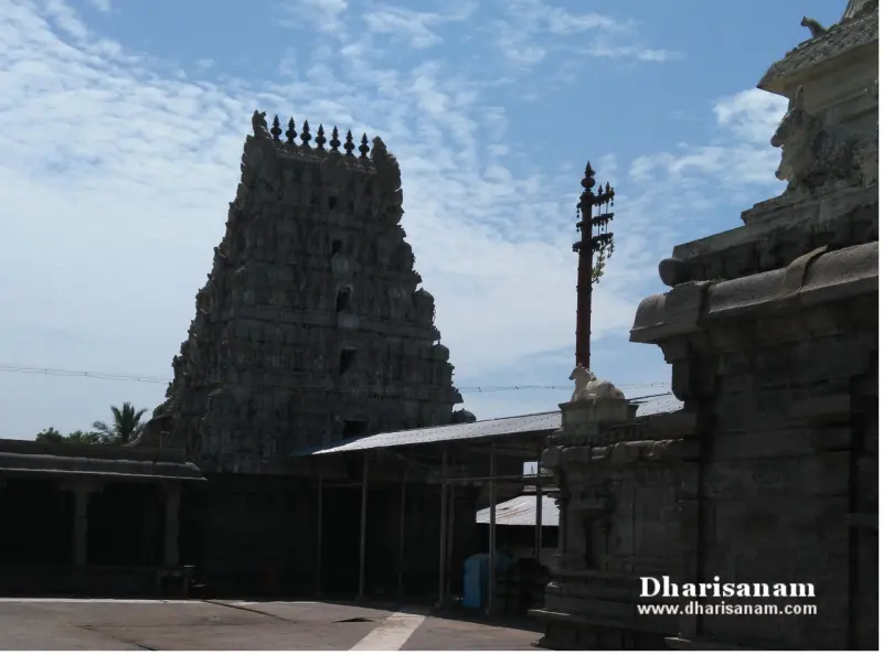 Dark stone tower on the left, a flagstaff with a small Nandi at its base and a carved wall on the right