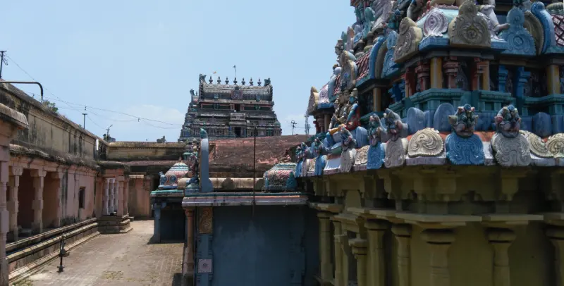 A paved corridor on the left and a painted tower wall on the right, with a gopuram in the distance.