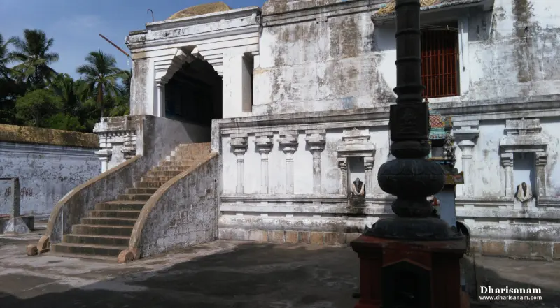 A flight of stone steps with sloping sides rises to an arched doorway of a white building, with a flagstaff at right