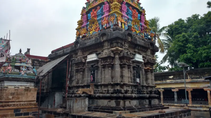 A brightly painted tower rises over a weathered stone structure, with trees behind.