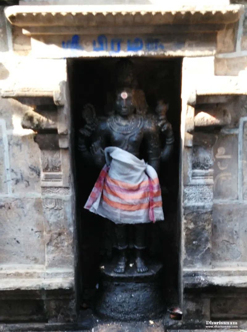 A standing dark idol with a cloth at the waist in a stone niche, with a Tamil name above it