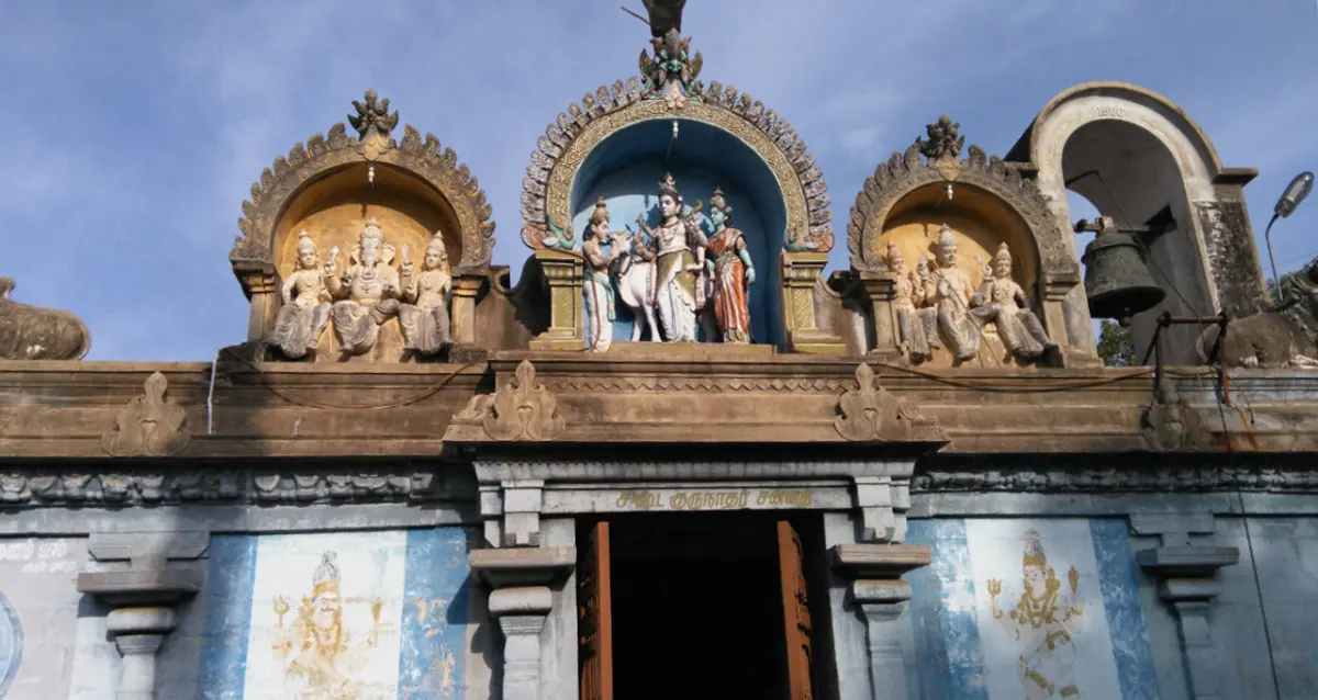 Colourful stucco figures in three niches above a temple doorway, with a bell hanging in an arch to the right