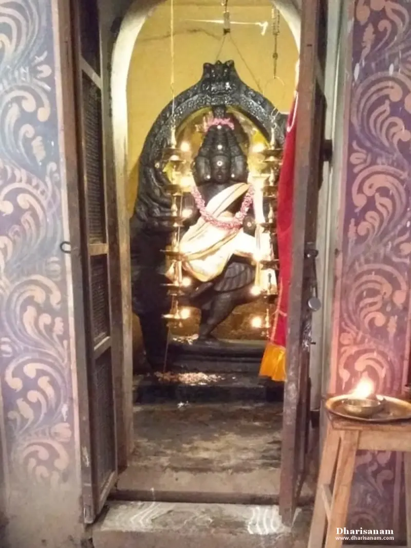 A tall dark idol with several faces framed by an arch and rows of lamps, seen through a shrine doorway