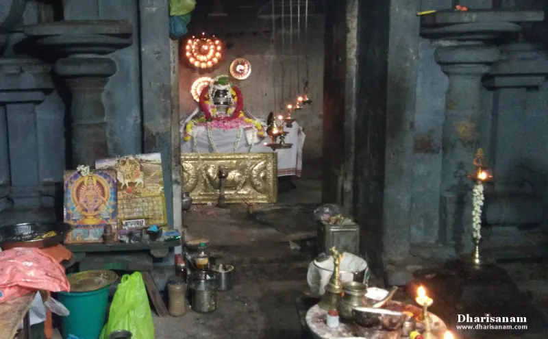 A garlanded lingam under hanging lamps seen through a dim doorway, with puja items in the foreground