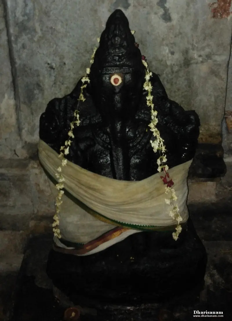 A seated black stone idol with a white cloth tied around it and two garlands of white flowers