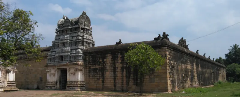 A long stone temple wall with small figures along its top and a carved gateway tower at the left end.