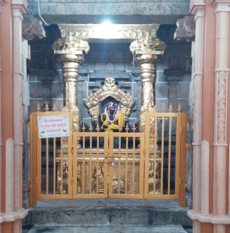 An idol garlanded in yellow cloth beneath a golden arch and pillars, behind an orange gate.