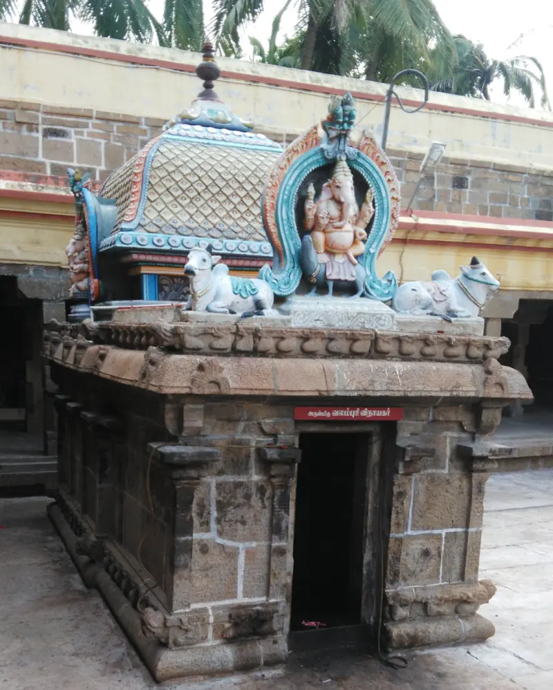 Small stone shrine with a red name board and a Vinayakar figure and two bulls on its roof