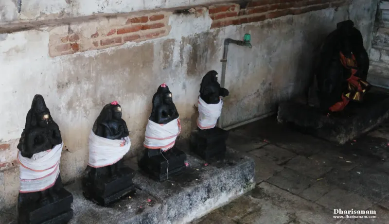 Four small black stone idols in white cloths on stone bases along a wall, with a larger idol on a platform at right.