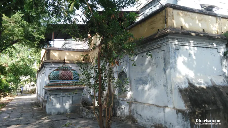 A shrine with a colourful dome at the end of a paved path along a whitewashed wall, trees overhead