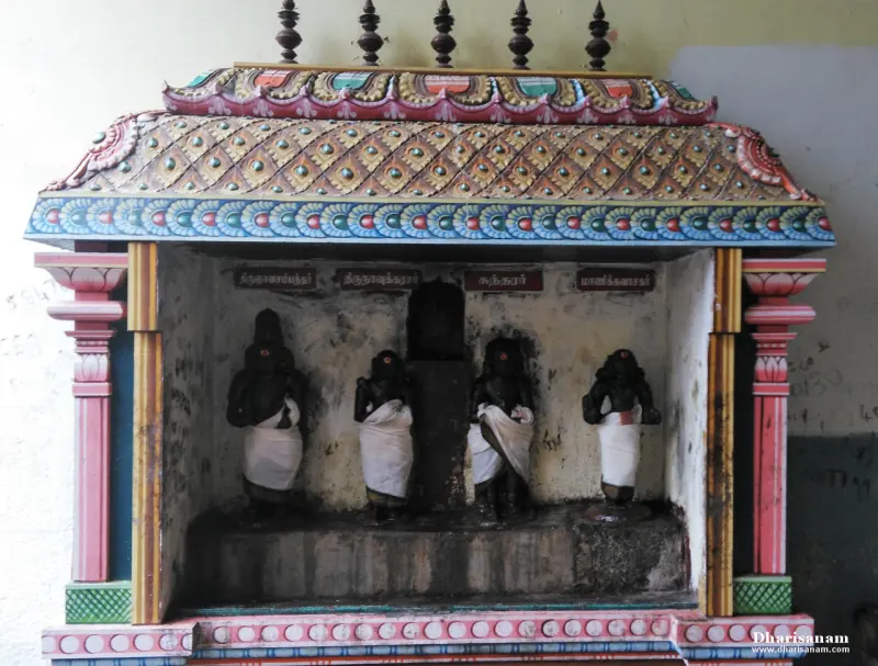 Four dark idols in white cloth stand in a painted shrine, each with a name plate above