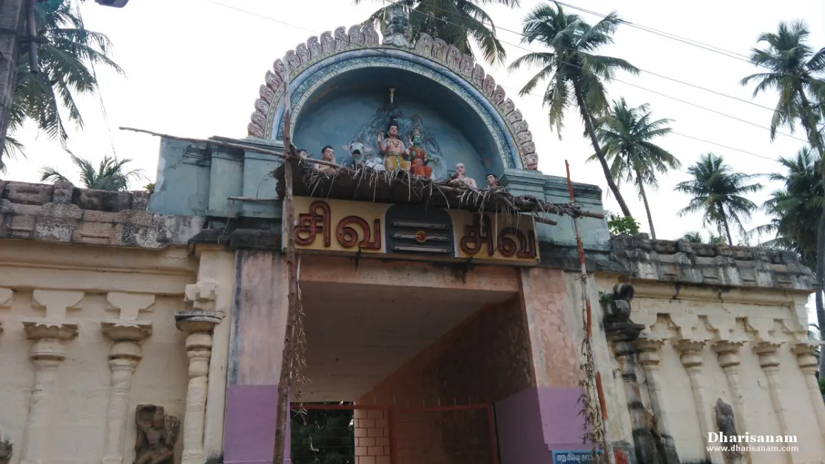 An entrance gateway under an arch with coloured figures of Shiva and Parvathy, a name board and palm trees