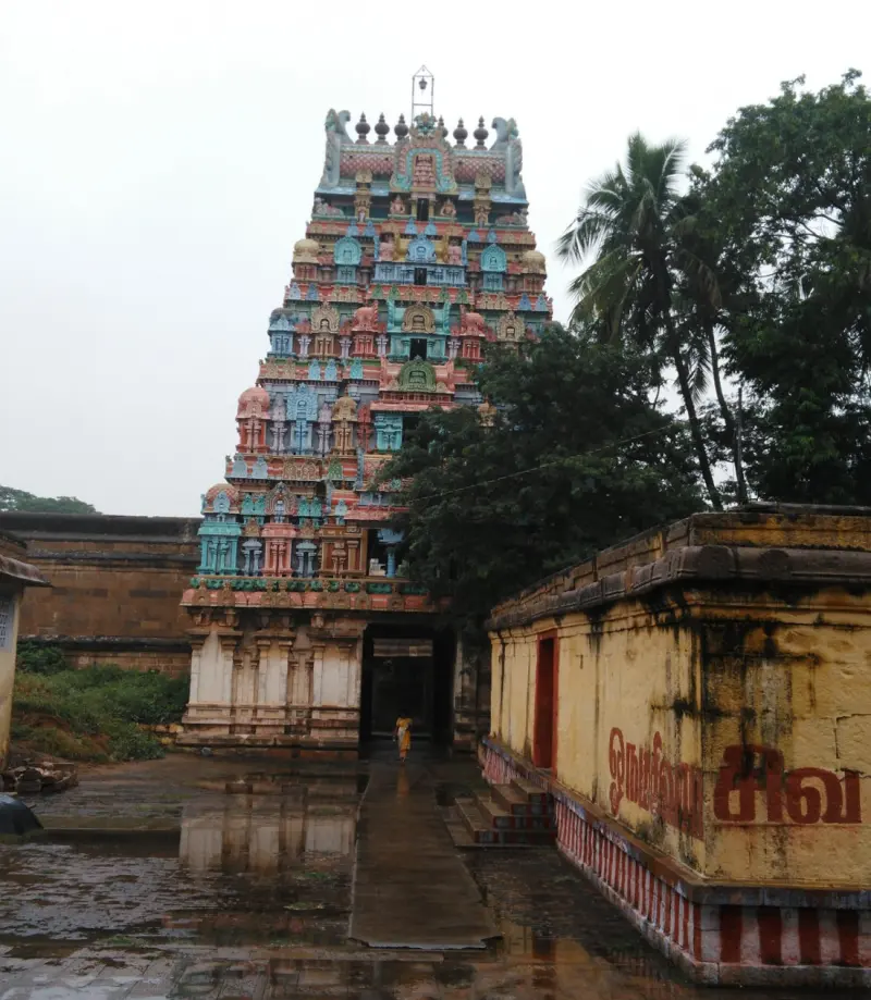 A tiered painted tower rises behind a wet stone courtyard, with a yellow wall on the right.