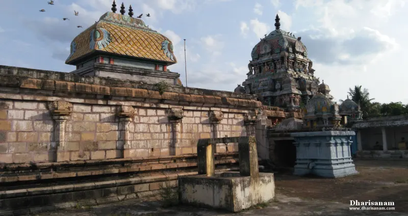 A stone wall with carved pilasters, a well-like stone structure and towers in the distance.