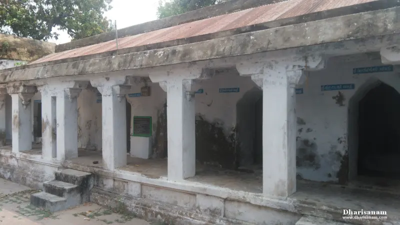 Open hall with white pillars and a tin roof, with blue Tamil name boards on the back wall