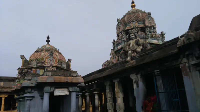 Two domed shrine roofs with sculpted figures beside a long pillared corridor.