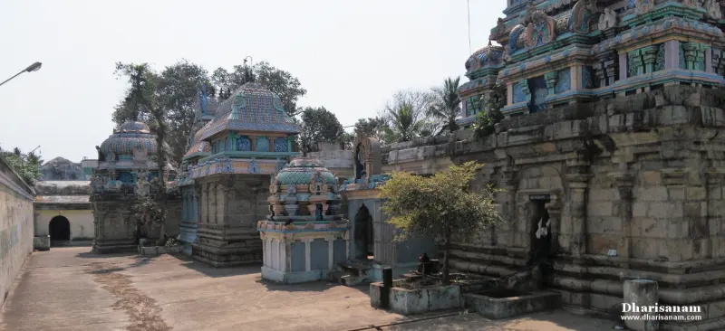 A paved temple corridor lined with small domed shrines and stone walls under a pale sky