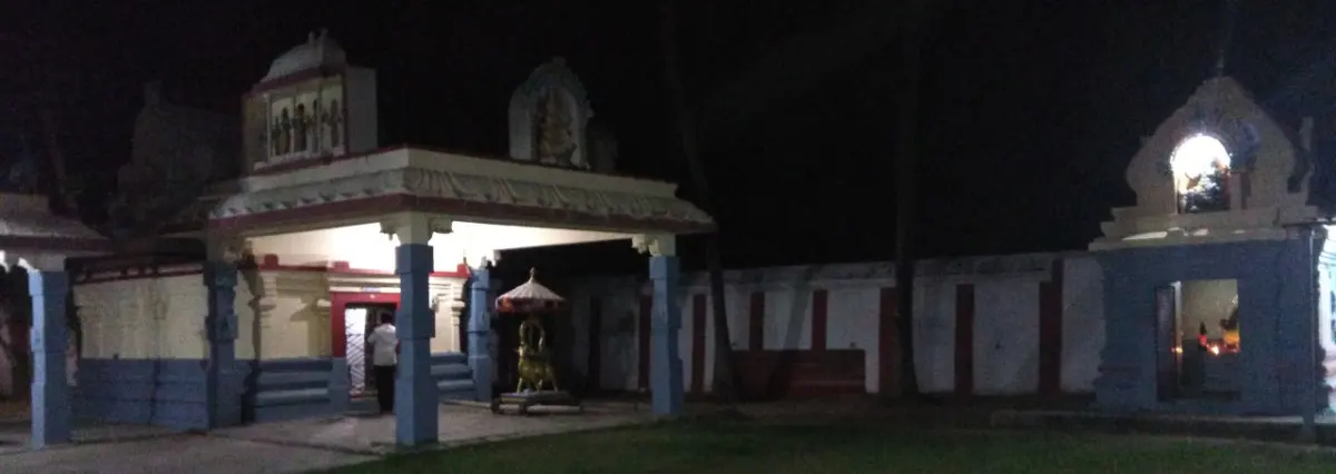 A pillared porch and a low white compound wall with a small gateway, lit at night