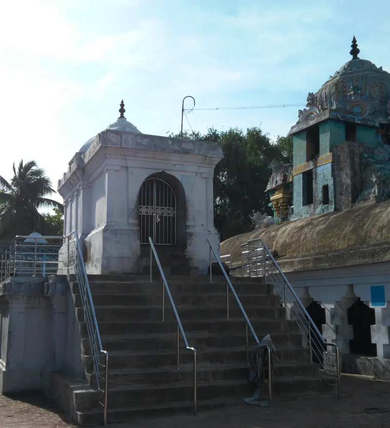 A white shrine with a barred arched door at the top of a wide flight of steps with steel railings.