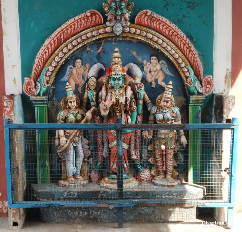 Three painted idols behind a wire grille: a central goddess with two attendants, one holding a veena