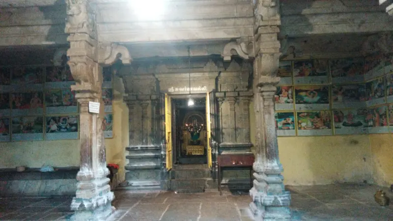 Rows of small coloured paintings on both walls of a stone hall, with the lit sanctum doorway in the middle.
