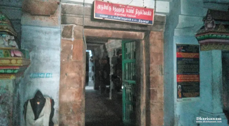 Stone doorway with a green gate and a red Tamil board above, leading into a dim passage