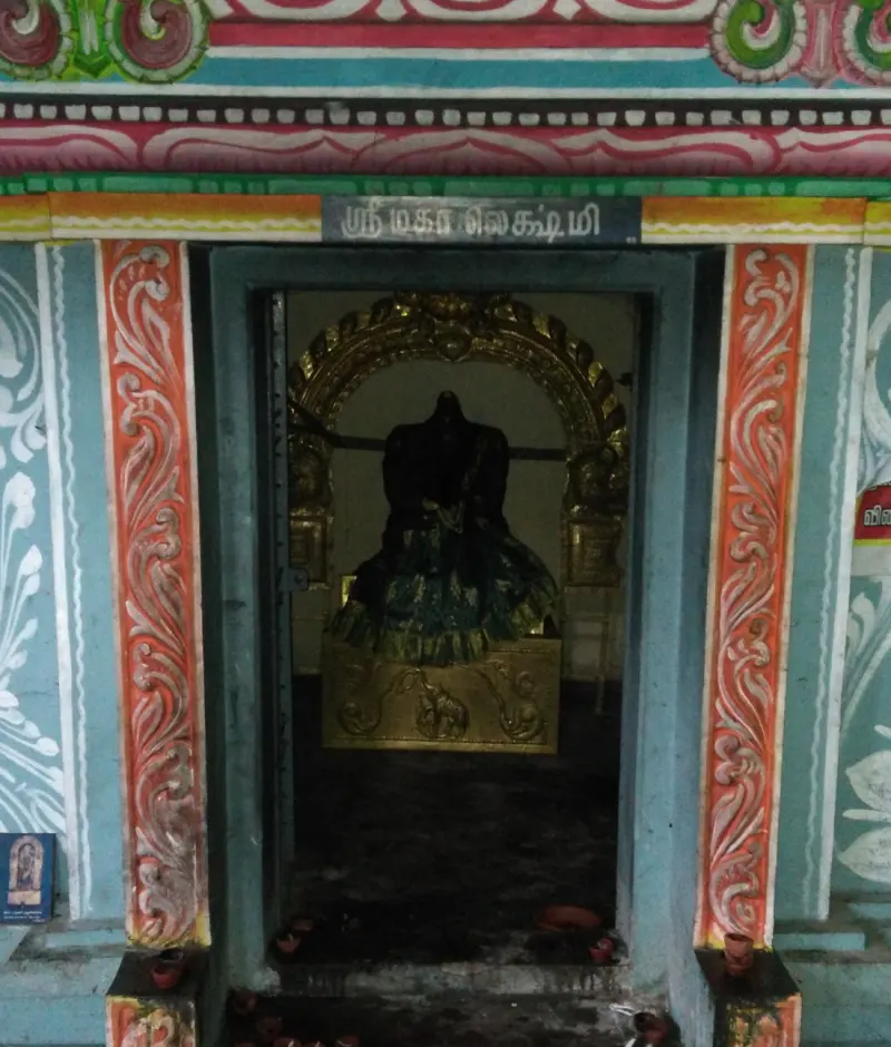 A small shrine with a dark idol in a green dress before a gilded arch; a Tamil board above names Mahalakshmi.