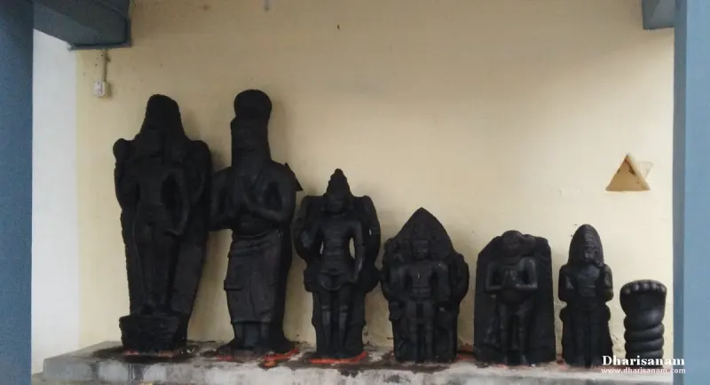 Several black stone idols and a coiled snake stone on a ledge against a pale wall