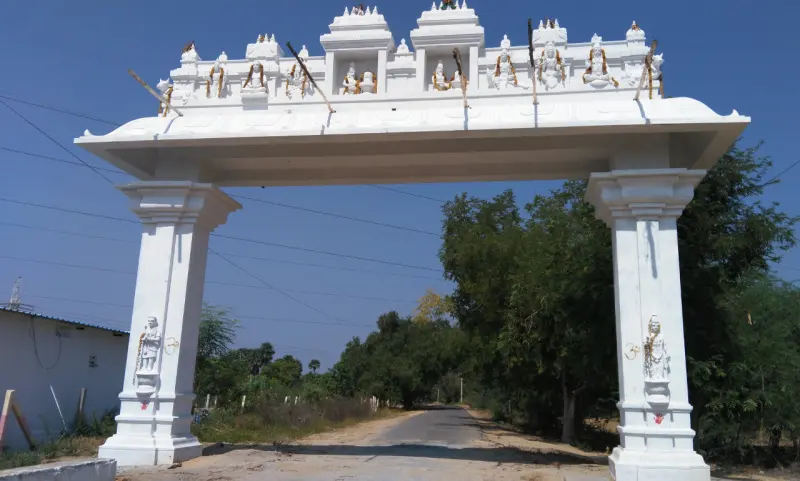 White roadside arch with small deity statues along its top, spanning a village road