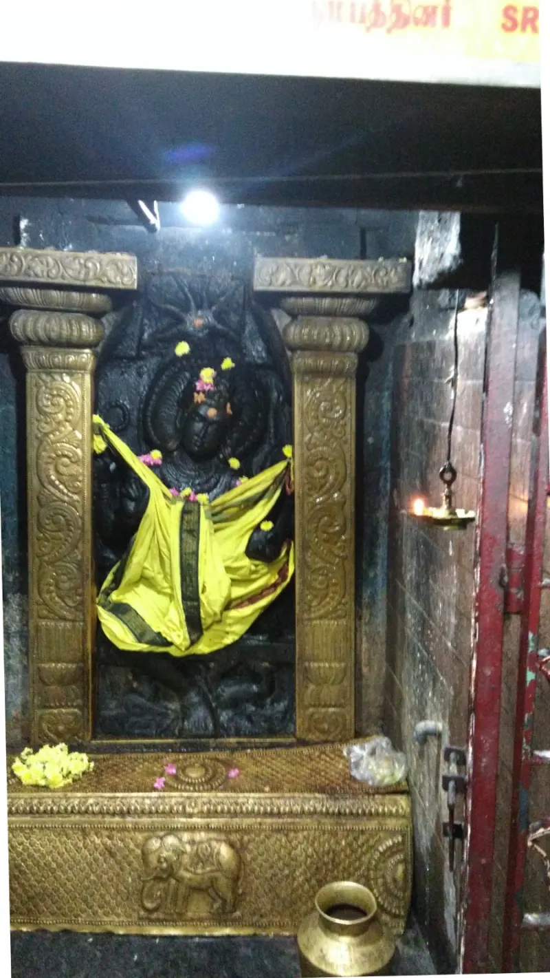 A dark stone god with flowers and yellow silk between brass pillars