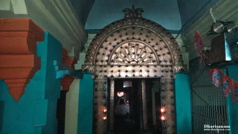 An ornate metal-clad arch over a doorway, with lamps burning and a deity faintly visible within.