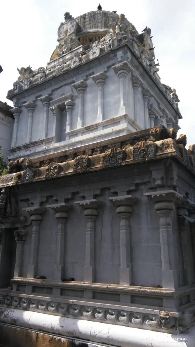 Grey-painted shrine walls with carved pilasters and a cornice rise to a tiered roof topped by a dome and finial