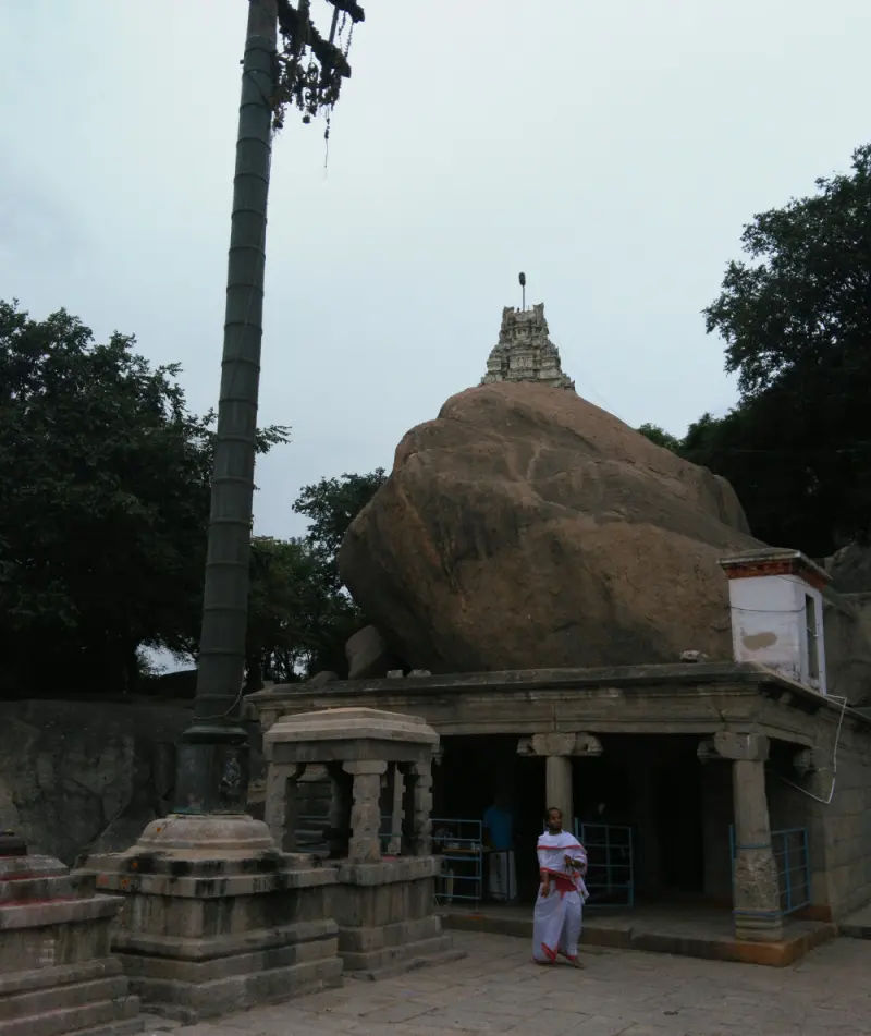 A small tower rises above a huge boulder over a stone hall, beside a tall flag post