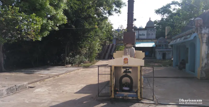A small open shrine with a lingam inside a niche, in front of a tall pillar and the temple buildings