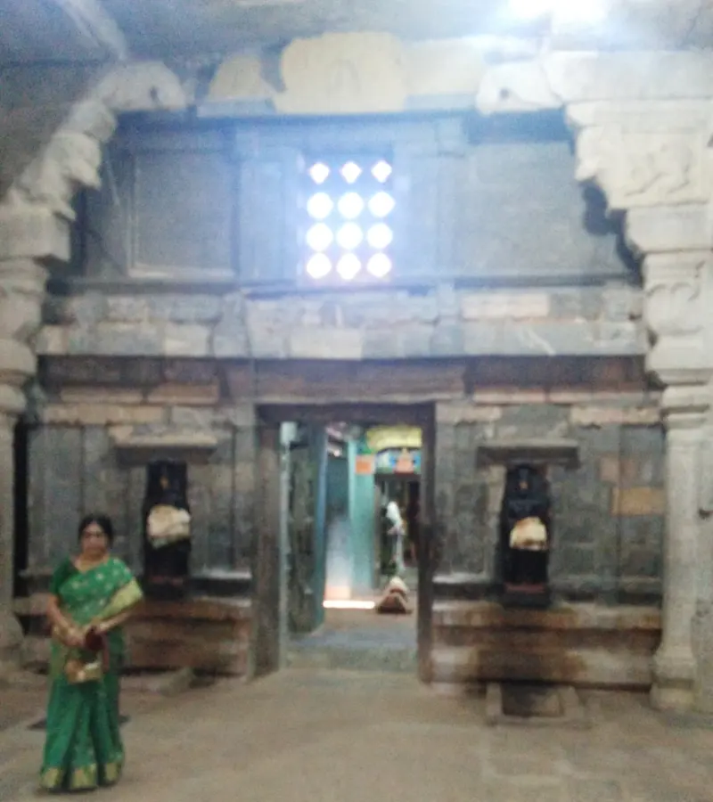 A doorway in a stone wall with a dark guardian idol in a niche on each side, and a woman standing at left.