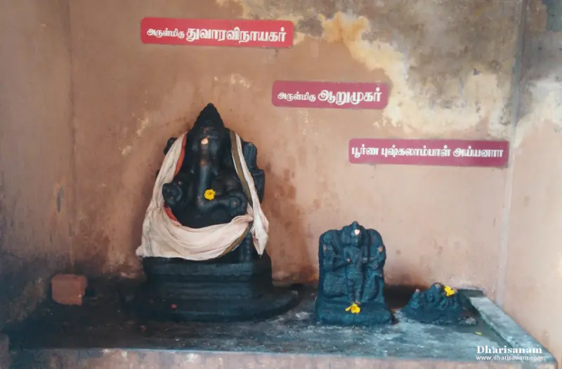 A seated Vinayakar and two smaller black stone idols on a ledge, each with a Tamil name board above