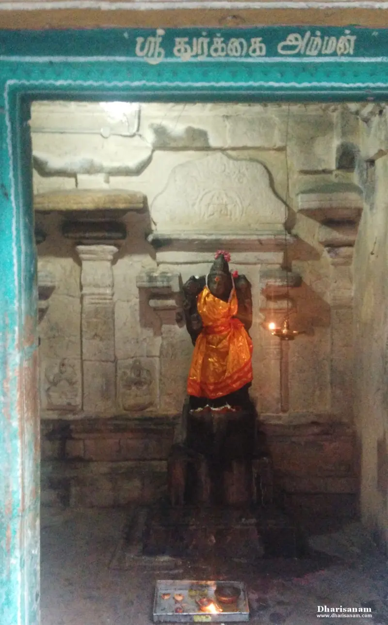 A stone image in an orange cloth stands in a niche framed in green, with offerings below.