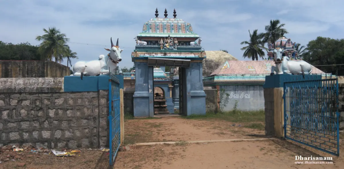 Blue gateway with a small tower between stone walls, with a white bull figure on each side and a dirt path leading in